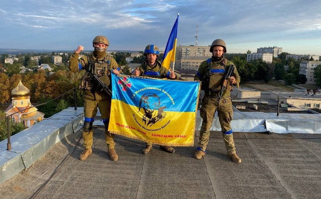Binh sĩ Ukraine giơ quốc kỳ trên nóc một tòa nhà ở Kupiansk ngày 10-9 - Ảnh: REUTERS