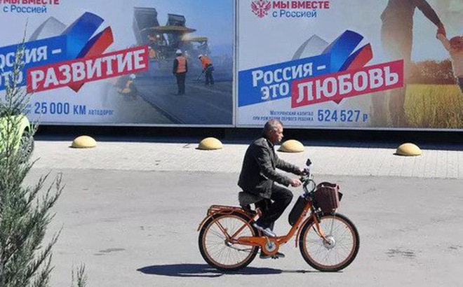 Một người dân thành phố Melitopol đạp xe ngang qua tấm áp phích với dòng chữ "Россия - это любовь" (Nước Nga chính là tình yêu) - Ảnh: RIA NOVOSTI