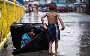 24h qua ảnh: Cậu bé trú mưa trong chiếc va li cũ