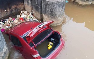 Ô tô màu đỏ nằm dưới mương, rác thải vây xung quanh khiến nhiều người tò mò